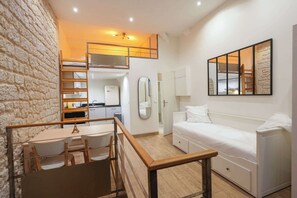 A compact hotel room with a bunk bed, a small kitchenette, a dining area with a table and chairs, and a large mirror. - Loft 2 BR Marais, Notre Dame AC by LCC Agency (Paris)