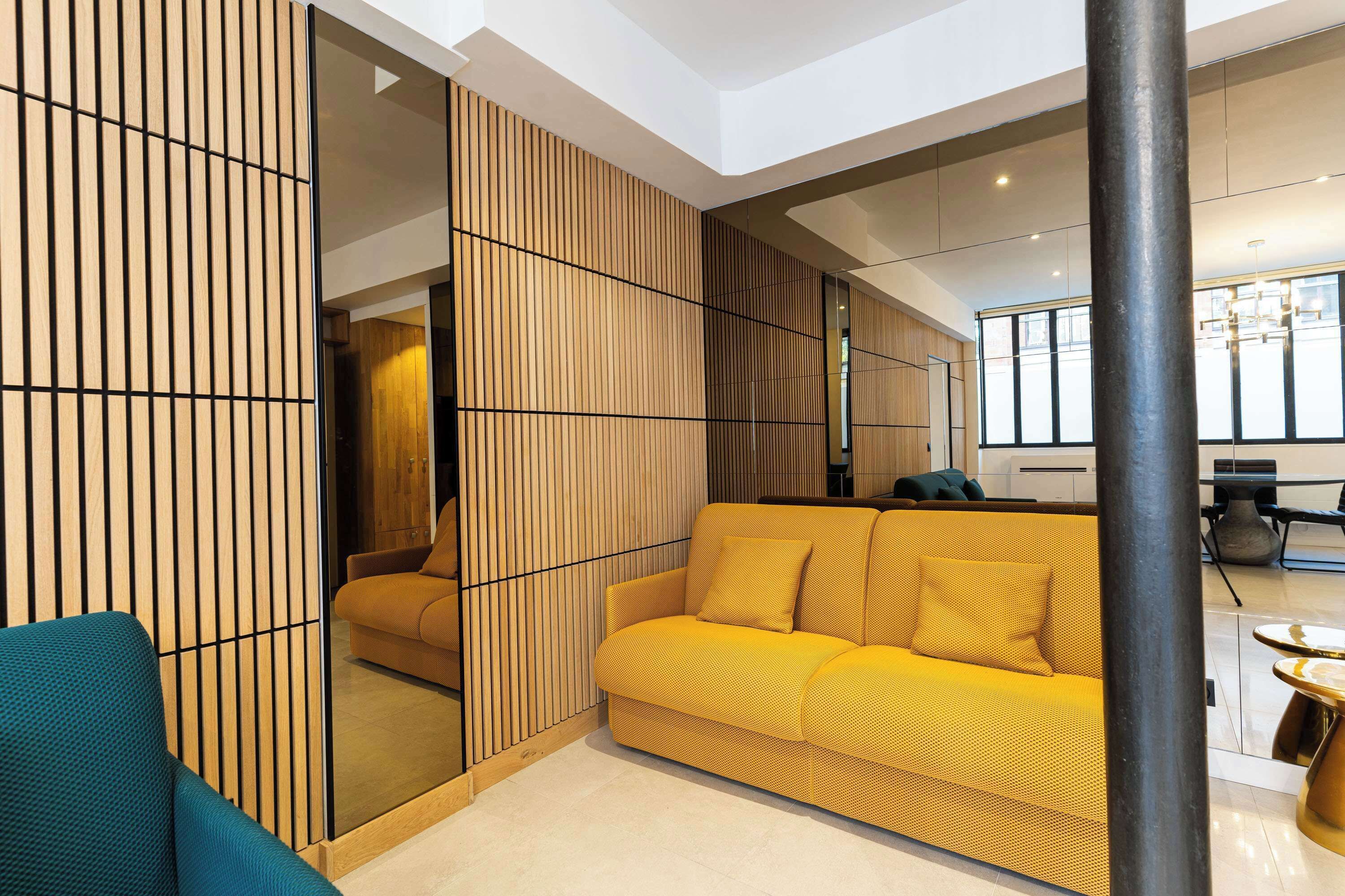 Un salon moderne avec un canapé jaune, un fauteuil turquoise et une cloison en bois.