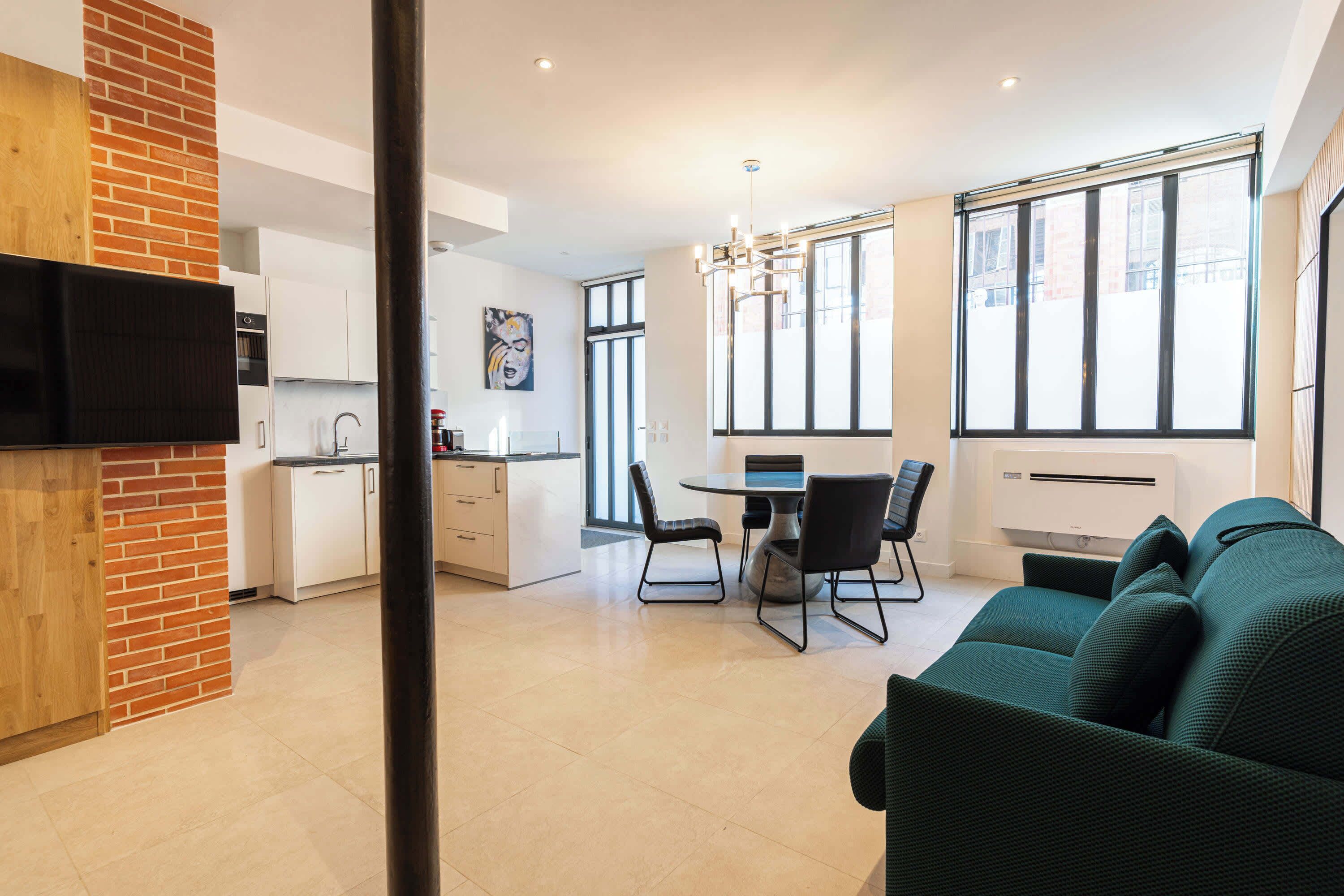 Une cuisine moderne avec des meubles blancs, un mur d’accent en briques et un coin repas comprenant une table et des chaises.