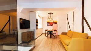 A modern living room with a wooden floor, a yellow sofa, a dining area with a table and chairs, and a kitchen in the background. - Loft 1 BR Marais, Notre Dame AC by LCC Agency (Paris)
