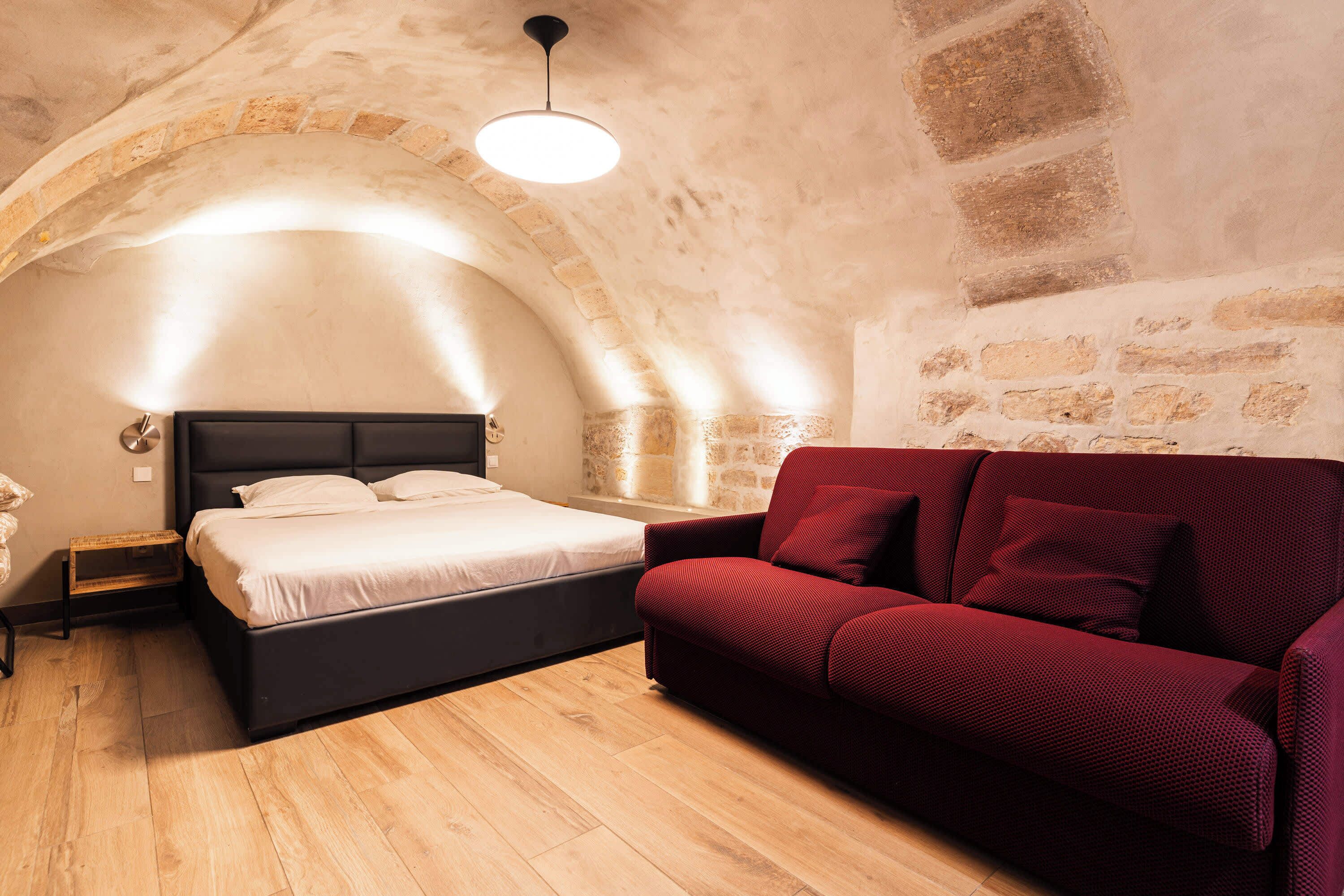 A bedroom with a bed, a red sofa, a nightstand, and a lamp.