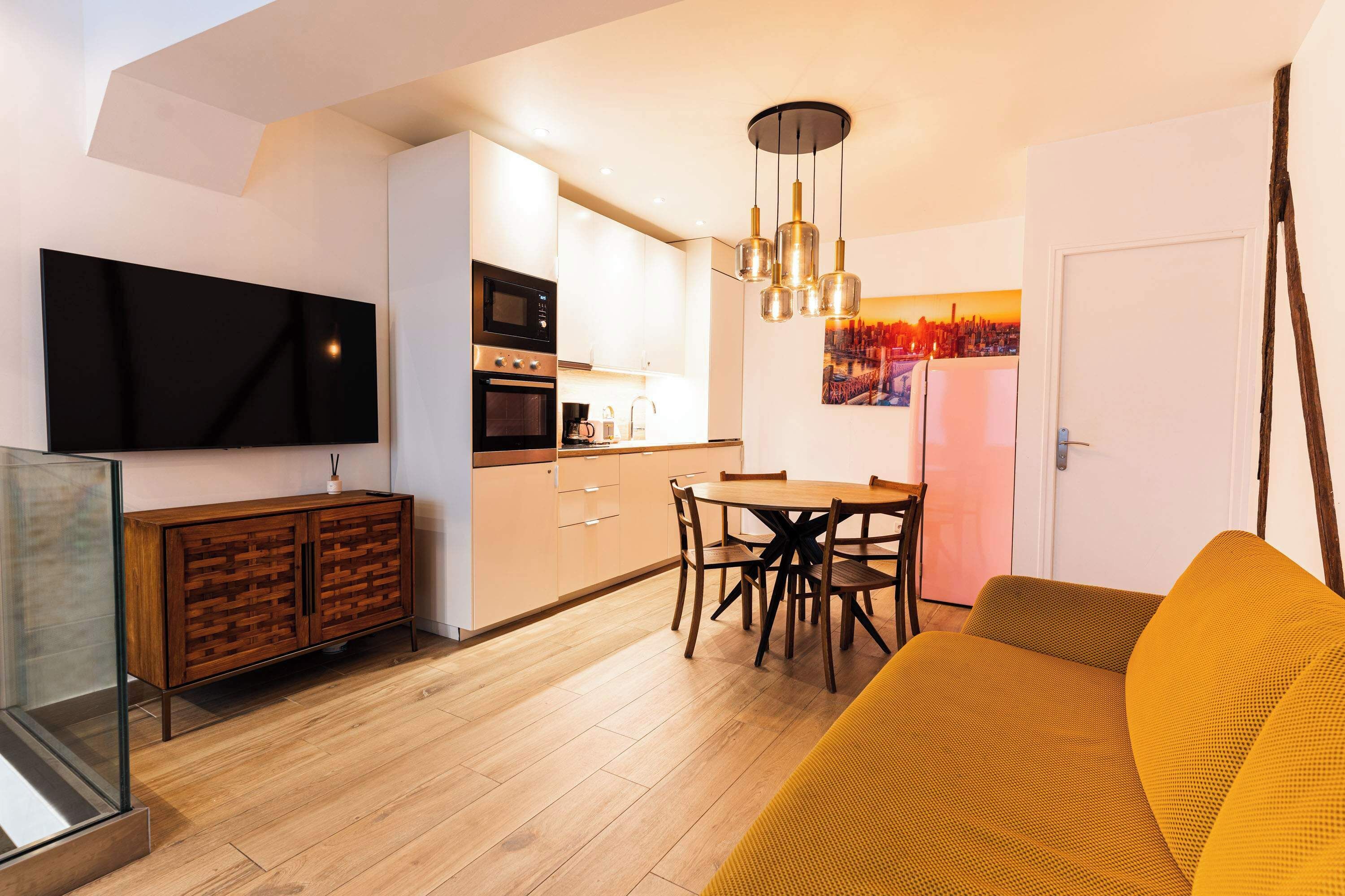 A modern kitchen with a dining area, a flat-screen TV, and a sofa.