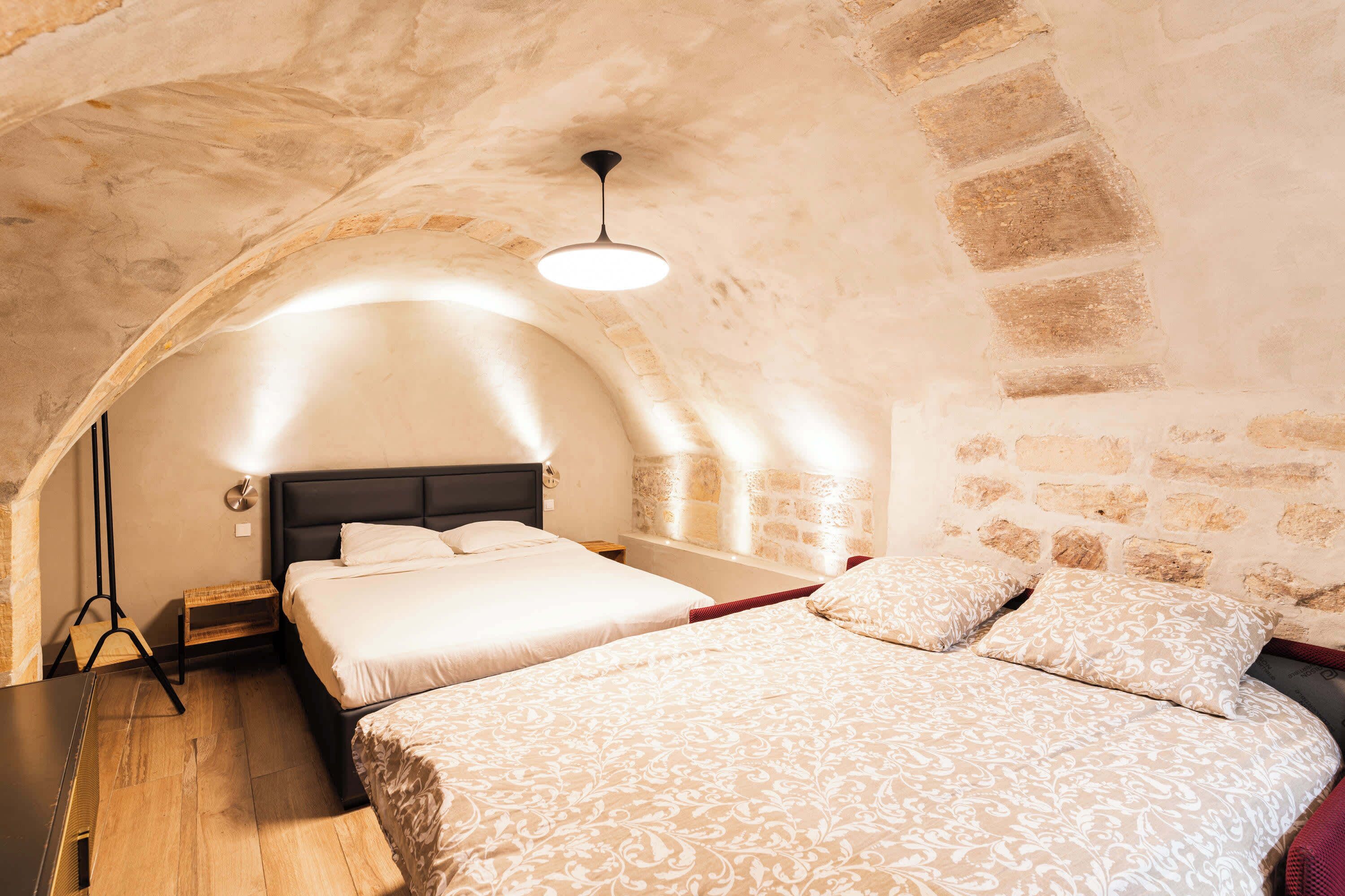 Um quarto acolhedor, com teto abobadado, uma cama grande, piso de madeira e paredes de pedra.