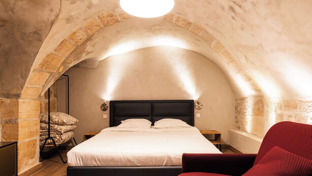 A bedroom with a bed, a red chair, and a stone archway. - Loft 1 BR Marais, Notre Dame AC by LCC Agency (Paris)
