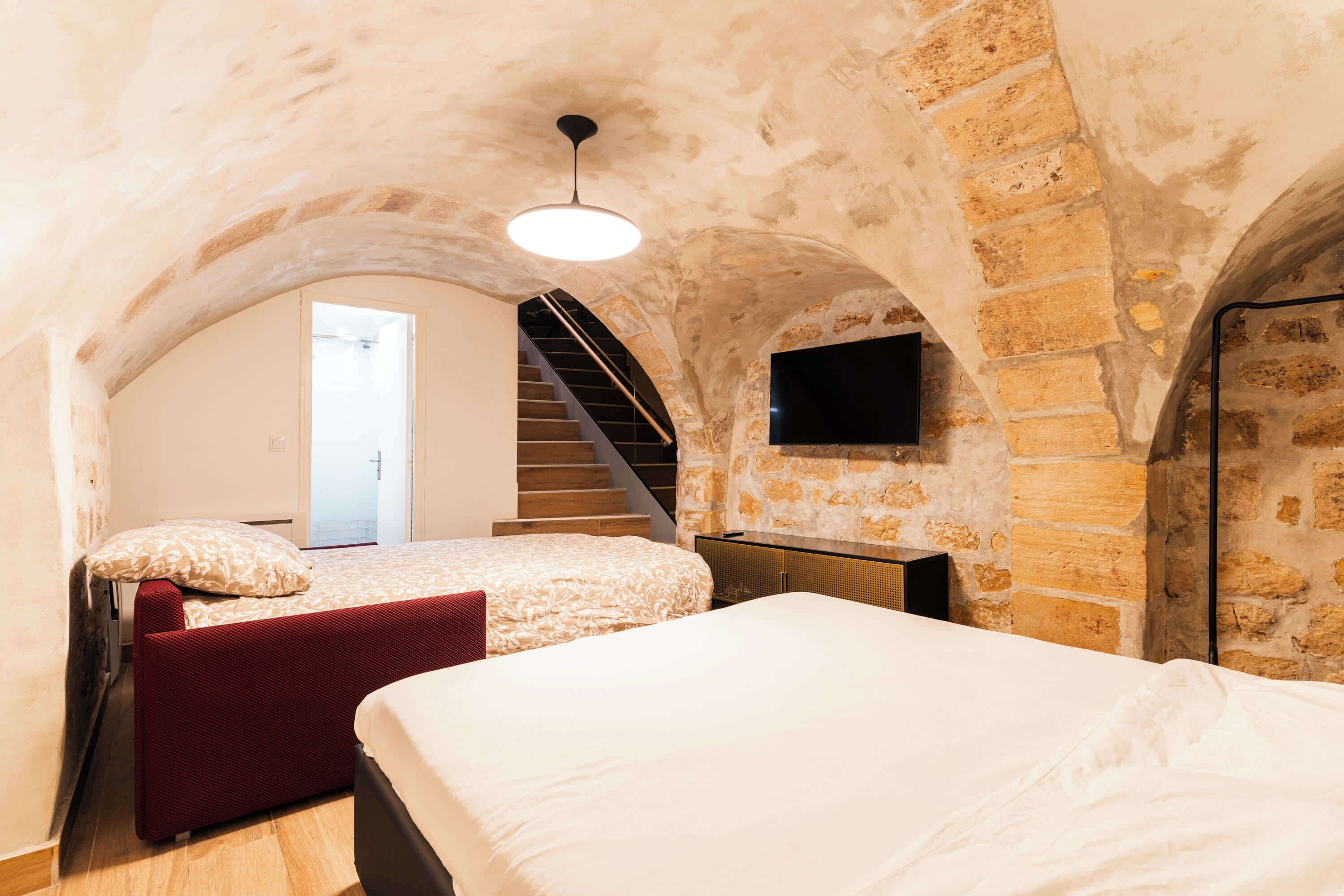 A bedroom with two beds, a staircase, and a TV mounted on the wall.