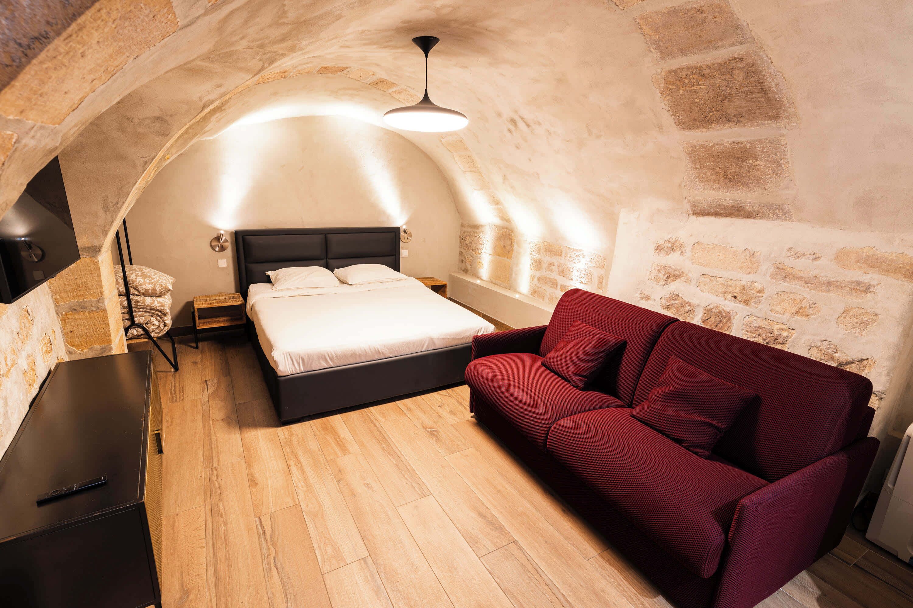 Une chambre à coucher avec un lit, un canapé rouge, un bureau et un mur en pierre.
