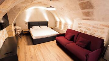Une chambre à coucher avec un lit, un canapé rouge, un bureau et un mur en pierre.