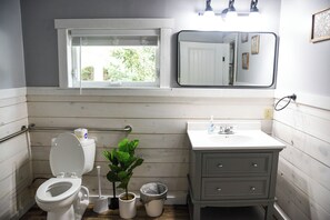 Et badeværelse med toilet, håndvask, spejl og vindue.