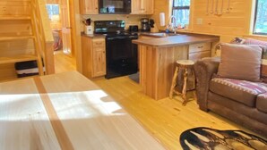 A wooden cabin interior with a kitchen, dining area, and a cozy living space.