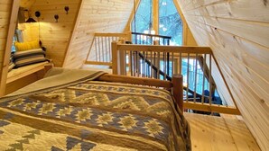 A high-ceilinged wooden room with a bed, a ceiling fan, and a window overlooking a forest. - The Treehouse near Cook Forest State Park (Leeper)