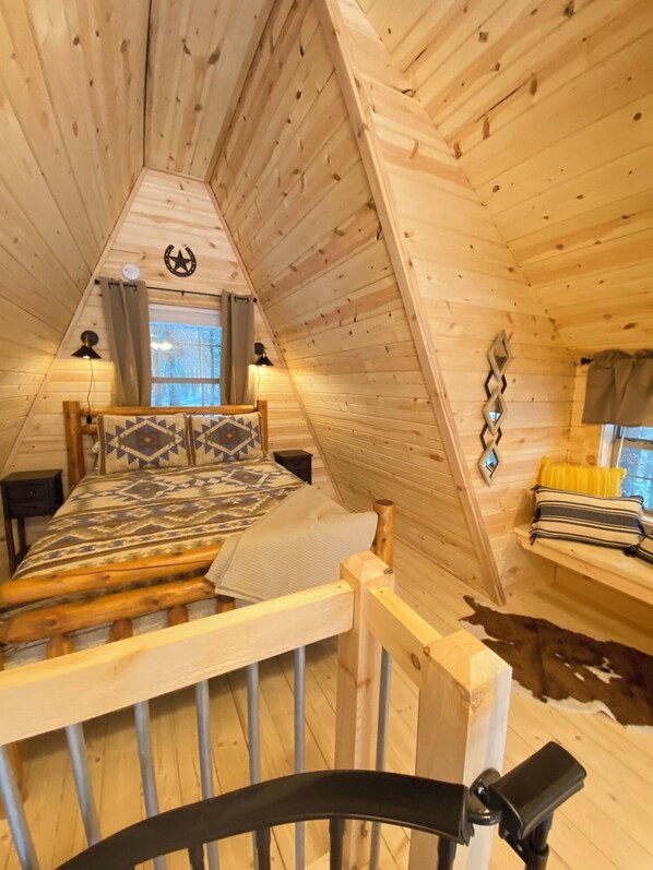 A cozy cabin interior with a loft bed, a small table, and a bench.