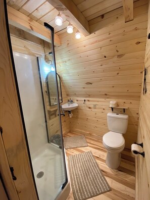 A wooden-paneled bathroom with a glass-enclosed shower, a white sink, and a toilet.