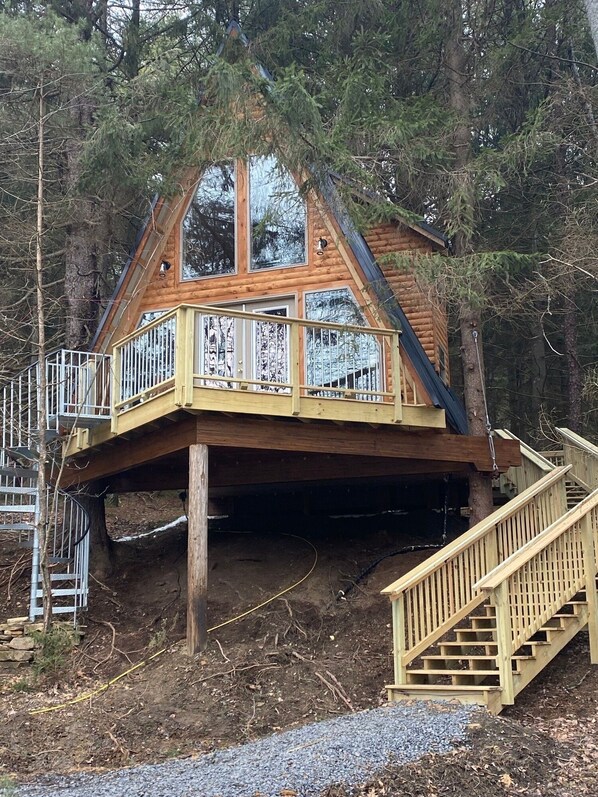 A wooden cabin with a deck and stairs, surrounded by trees.