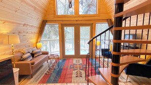 A spacious loft-style room with a wooden floor, a sofa, a dining table, and a staircase. - The Treehouse near Cook Forest State Park (Leeper)