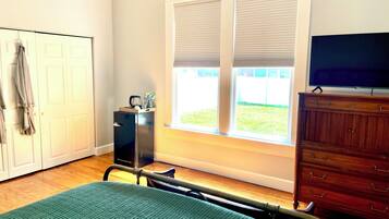 A bedroom with a bed, a dresser, a television, a window with blinds, and a door.