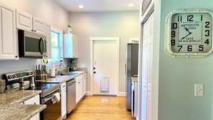 Una cocina moderna con armarios blancos, encimeras de granito, electrodomésticos de acero inoxidable y piso de madera.