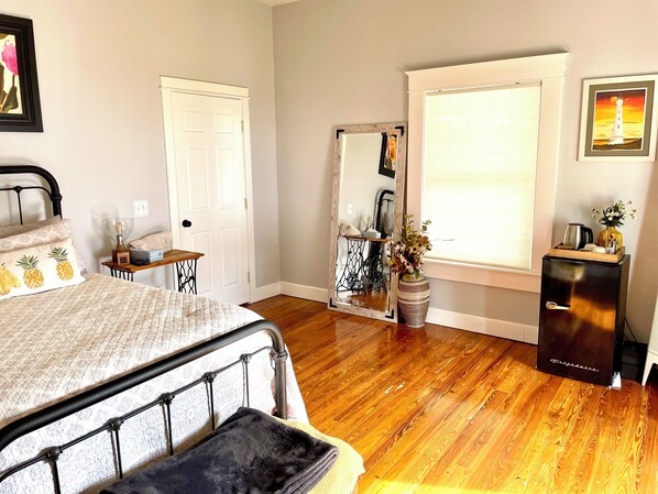Un dormitorio con cama, cómoda, espejo, ventana con persianas y una mesita de noche con lámpara.