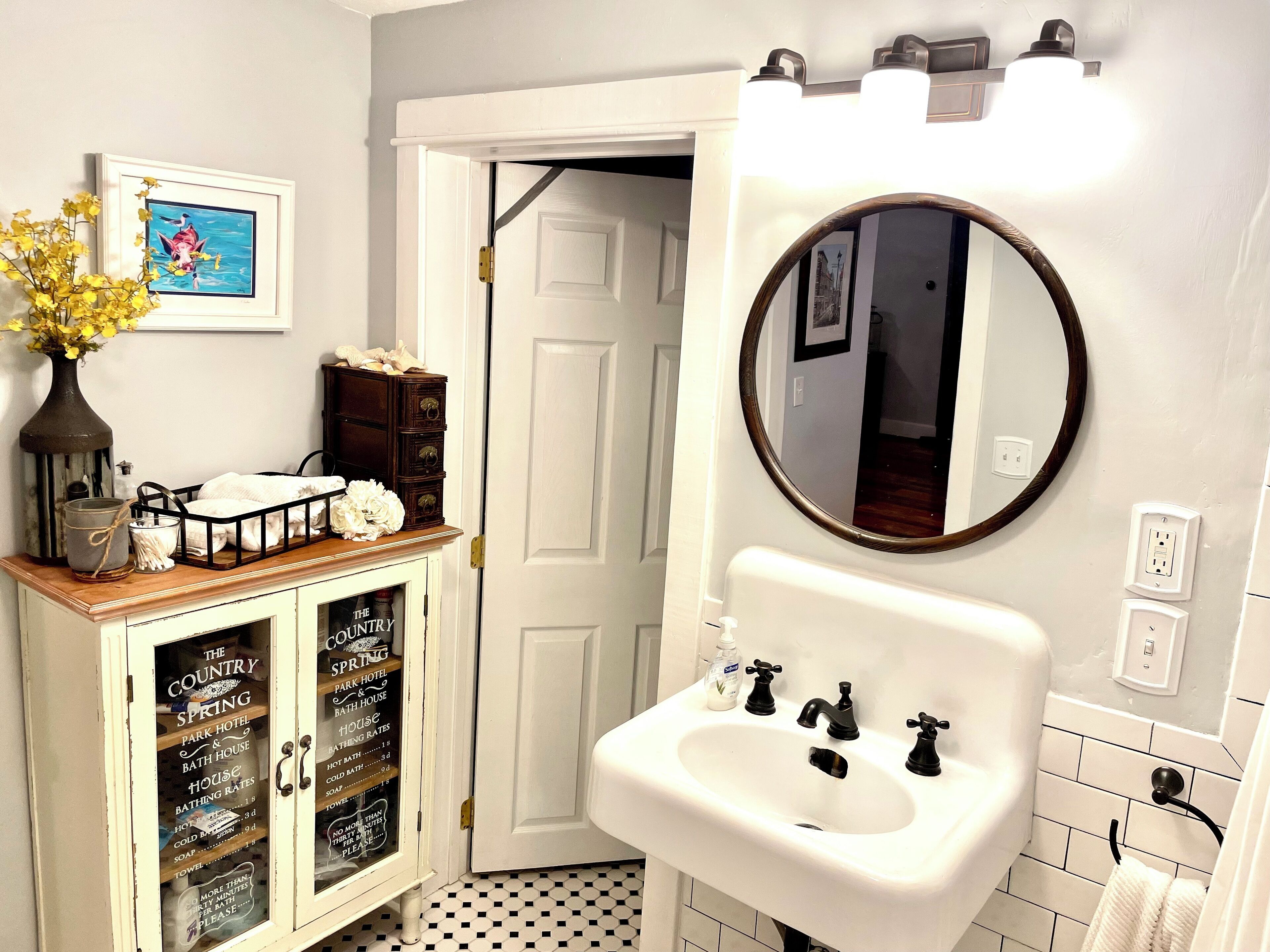 Une salle de bain avec un lavabo blanc, un miroir et un meuble sur lequel est affiché un panneau indiquant les tarifs du Country Spring Park Hotel & Bath House.