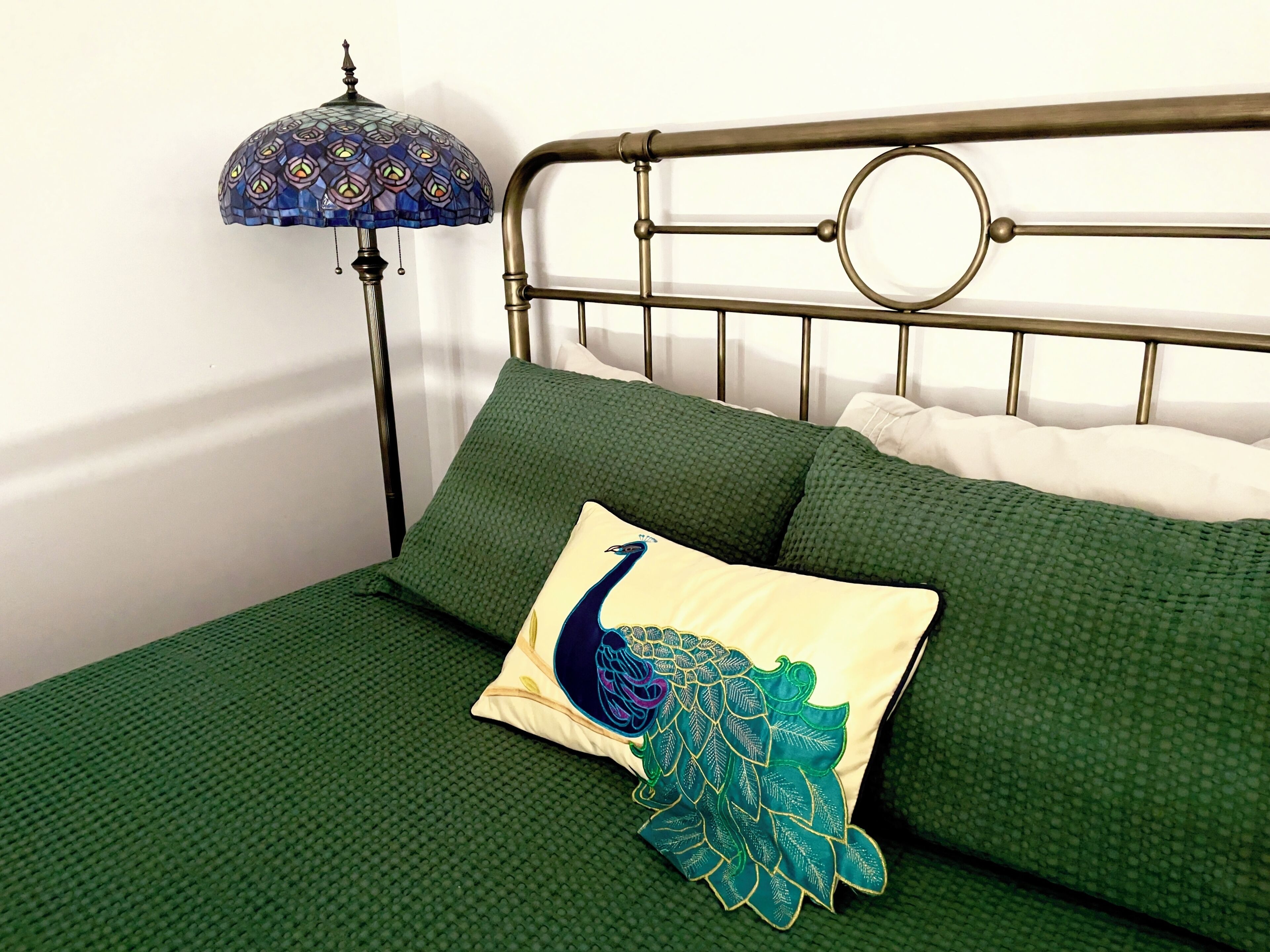 A bed with green bedding, a decorative pillow with a peacock design, and a blue patterned lamp.