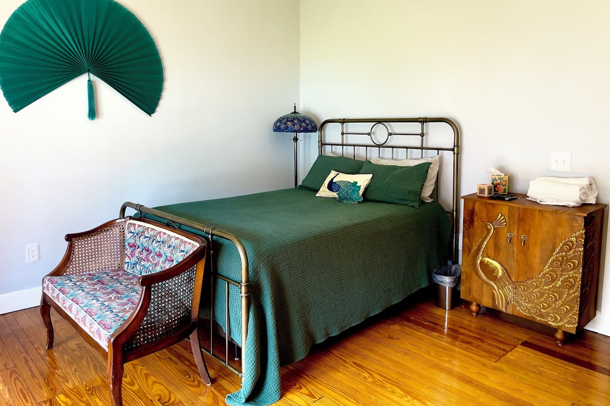 A neatly arranged bedroom with a bed, a chair, a cabinet, and a wall-mounted fan.