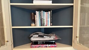 A white wooden cabinet with three shelves, a radio on the top shelf, and books on the middle shelf.