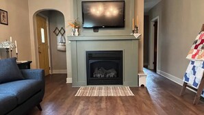A living room with a fireplace, a television mounted above it, and a chandelier.