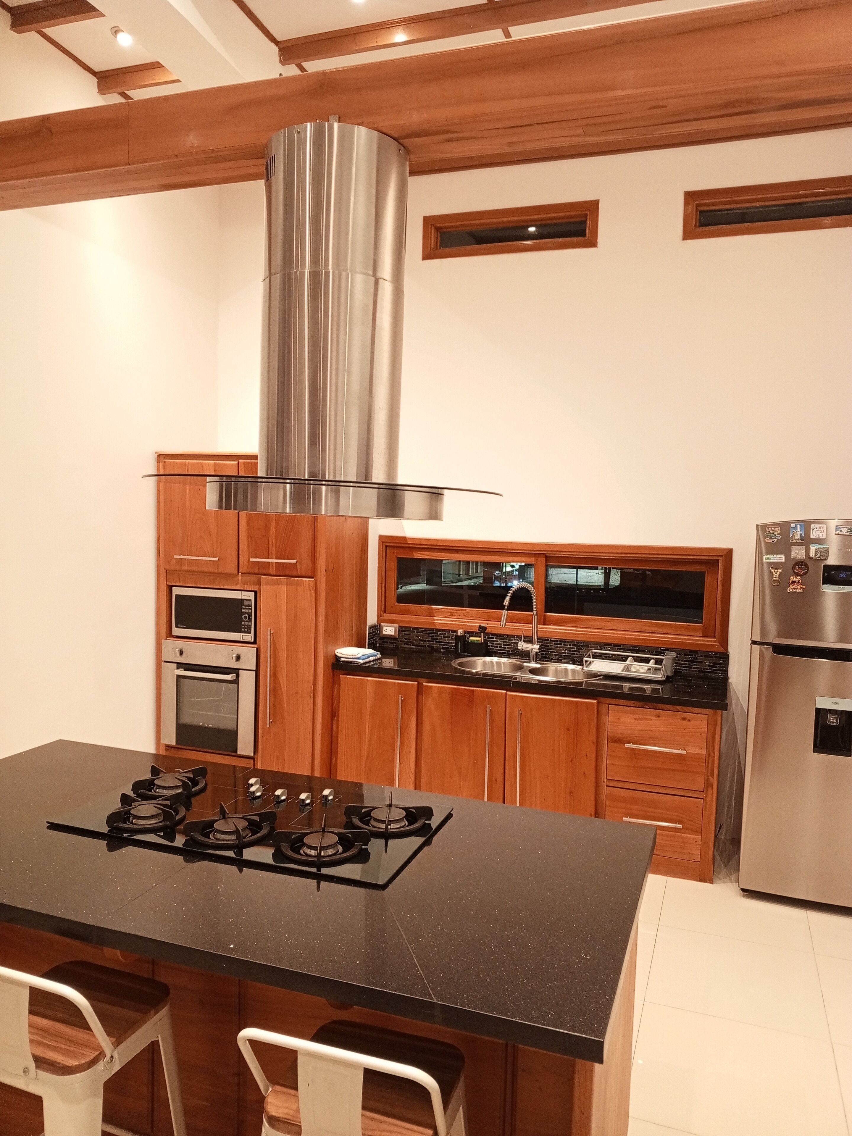 A modern kitchen with a central island, built-in oven, stainless steel appliances, and wooden cabinetry.