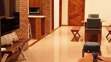A modern living room with a brick wall, a flat-screen TV, a wooden coffee table, and a dining area with a table and chairs.