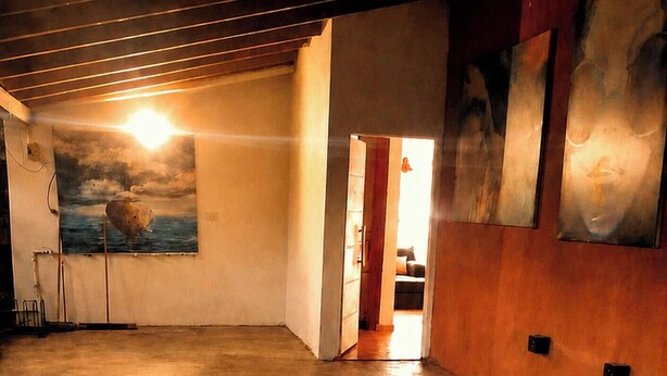 An interior space with a concrete floor, a ceiling with exposed beams, a door leading to another room, and a wall with abstract art. - Buenos Aires de Ezeiza Resort Vacacional - Departamento N°1 (La Unión)