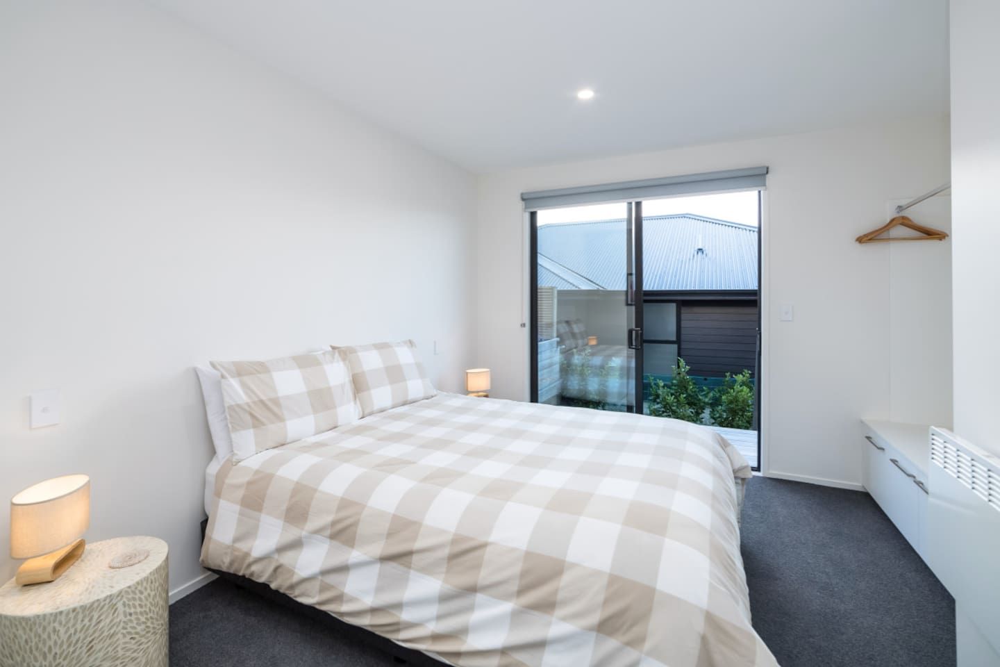 Un dormitorio con cama, lámpara de noche y vistas al exterior.