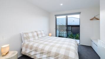 Un dormitorio con cama, lámpara de noche y vistas al exterior.