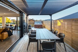 An outdoor patio with a wooden deck, a covered seating area, and a barbecue grill.