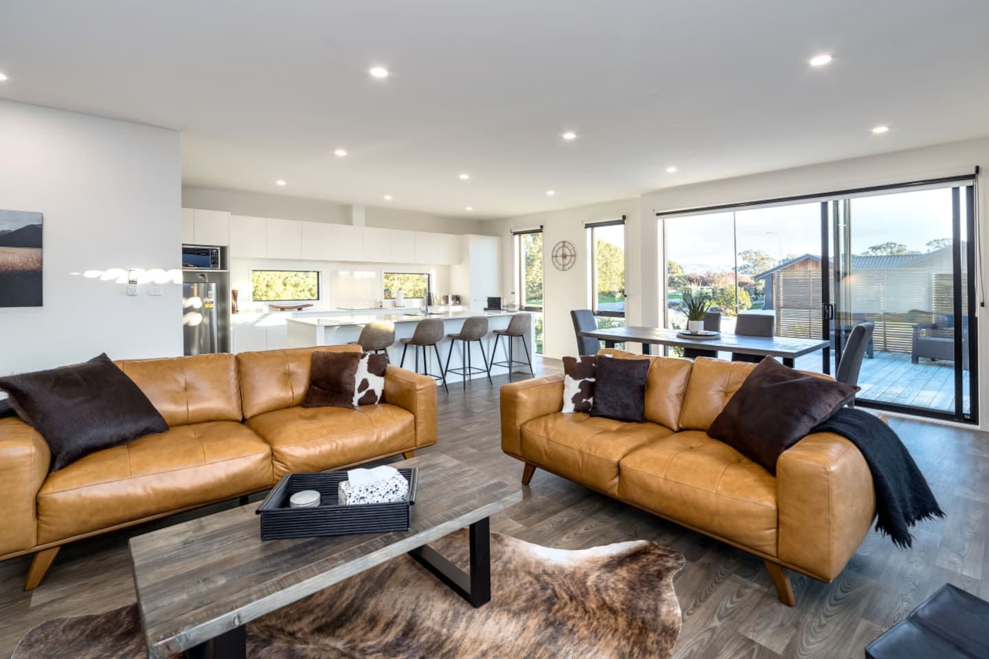A modern living room with two leather sofas, a coffee table, and a dining area with a large window.