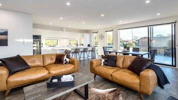A modern living room with two leather sofas, a coffee table, and a dining area with a large window.