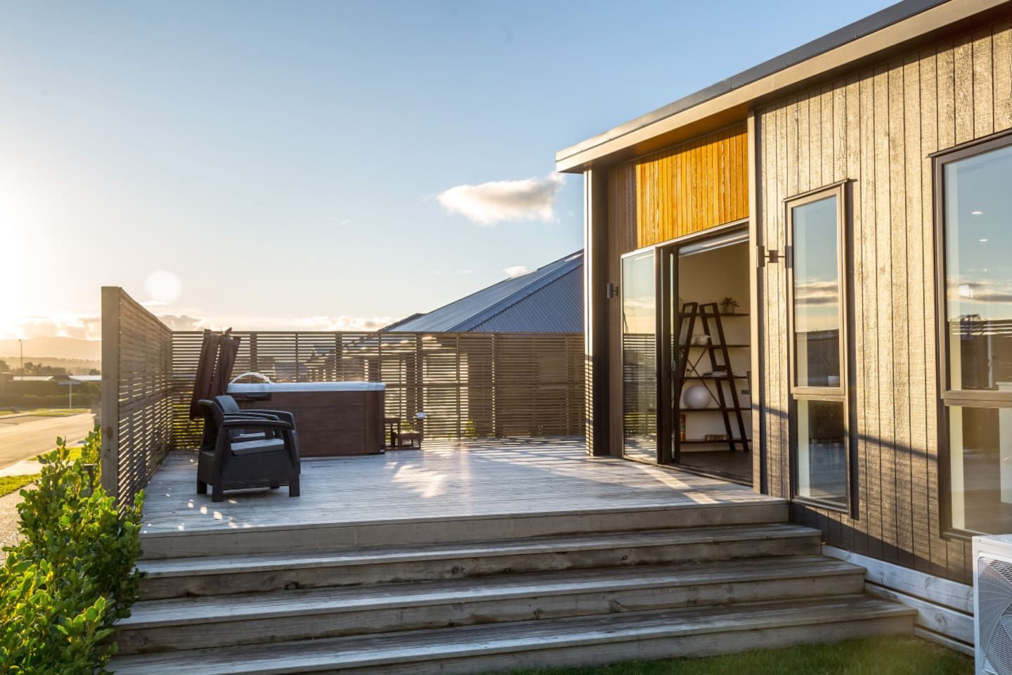 A modern outdoor patio with a barbecue area, steps leading to a wooden door, and a view of the surrounding landscape.