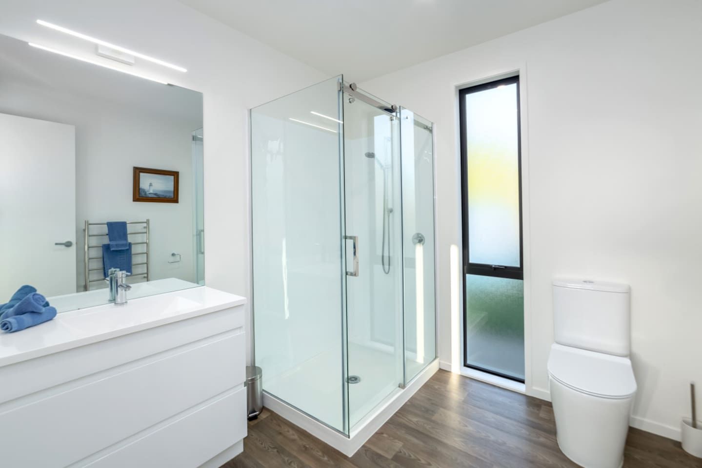 A modern bathroom with a glass shower enclosure, a white vanity, and a large mirror.