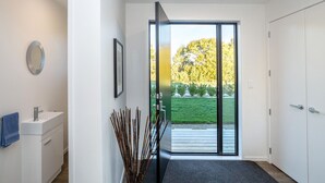 Een moderne badkamer met een witte wastafel, een spiegel en een deur die uitkomt op een balkon met uitzicht op een tuin en bomen.
