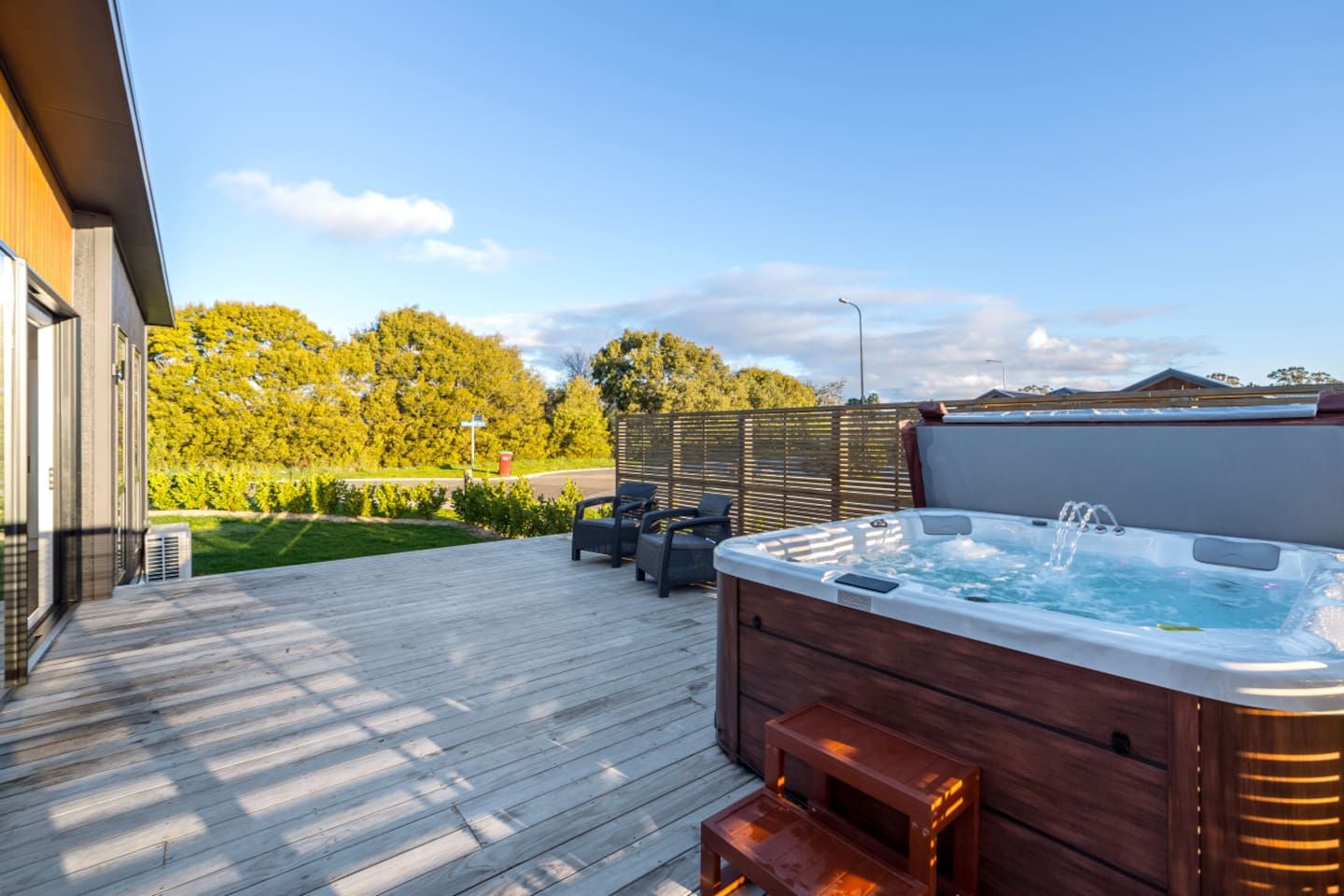 Una terraza de madera con jacuzzi, mobiliario exterior y vista a un paisaje verde.