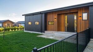 Een modern huis met twee verdiepingen, een donkere gevel, een houten voordeur en een klein terras.