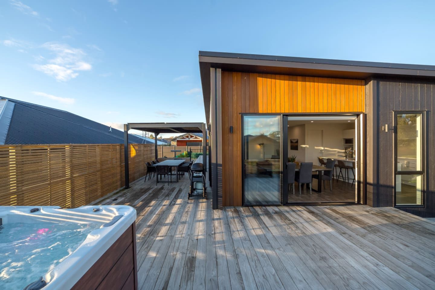 Una terraza moderna al aire libre con jacuzzi, suelo de madera y un área de estar cubierta.
