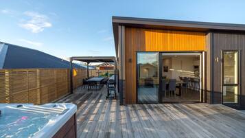 Una terraza moderna al aire libre con jacuzzi, suelo de madera y un área de estar cubierta.