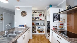A modern kitchen with granite countertops, white cabinetry, a built-in oven, and a microwave. There is a wooden floor and a hanging pendant light. - Michaelia House, Greytown (Greytown)