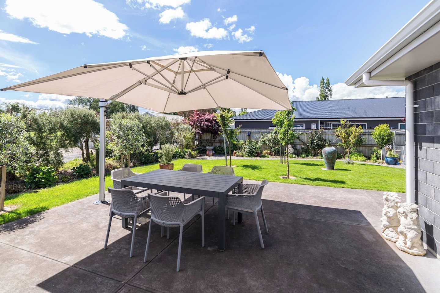 An outdoor patio with a table and chairs, a large umbrella, and a garden view.