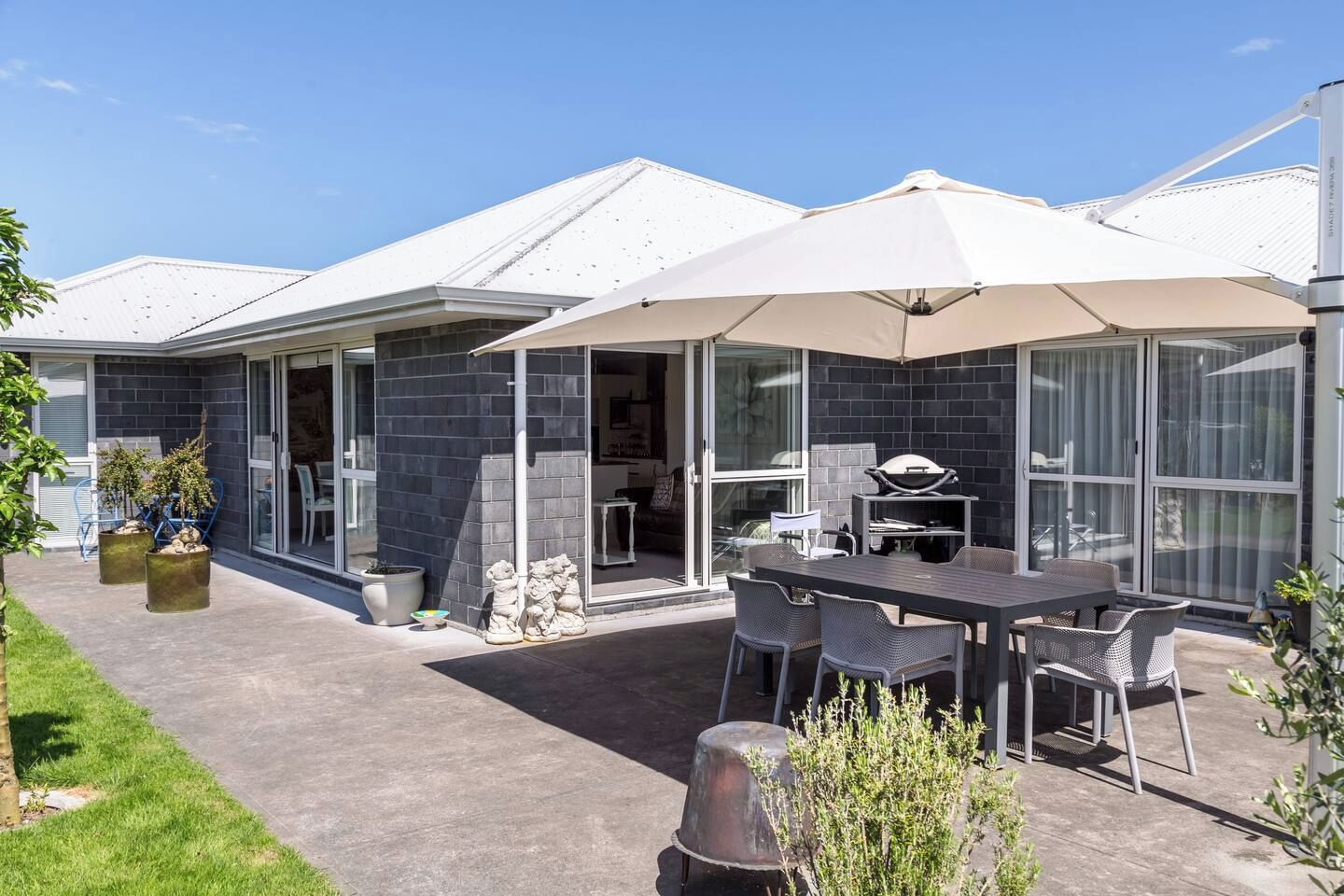 Ein moderner Außenbereich mit einer Terrasse, einem Esstisch und Stühlen, einem Grill und einem überdachten Sitzbereich.