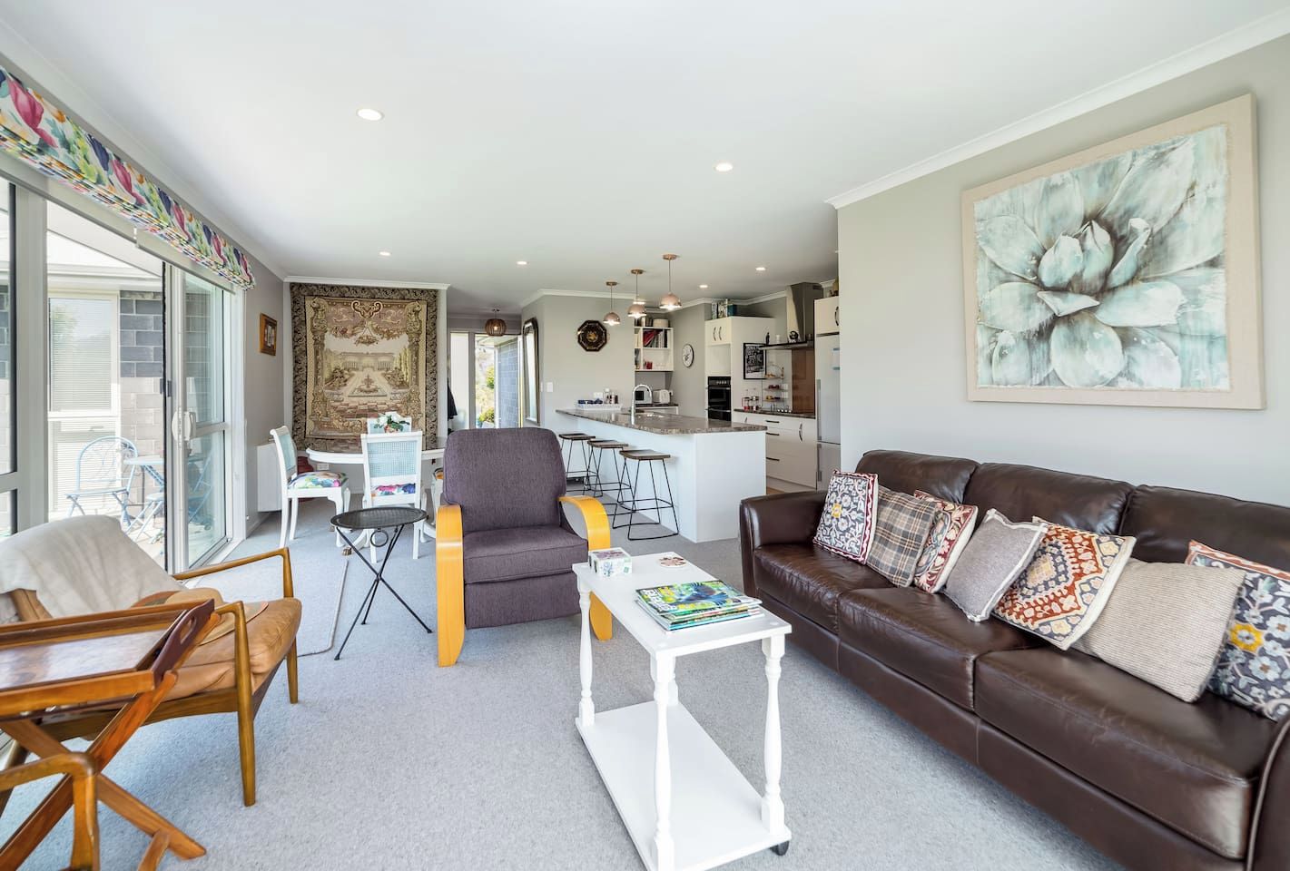 Ein modernes Wohnzimmer mit einem braunen Ledersofa, einem grauen Sessel und einem weißen Couchtisch. Es gibt einen Essbereich mit Tisch und Stühlen, und im Hintergrund befindet sich eine Küche.
