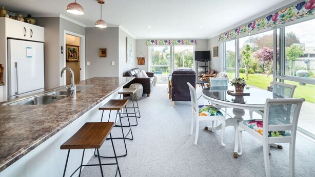 A modern kitchen with a central island, bar stools, and a dining area with a round table and chairs. - Michaelia House, Greytown (Greytown)