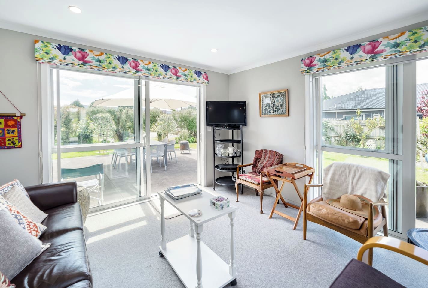 A spacious living room with a sofa, coffee table, and chairs, large windows with a view of the outdoors, and a television on a stand.