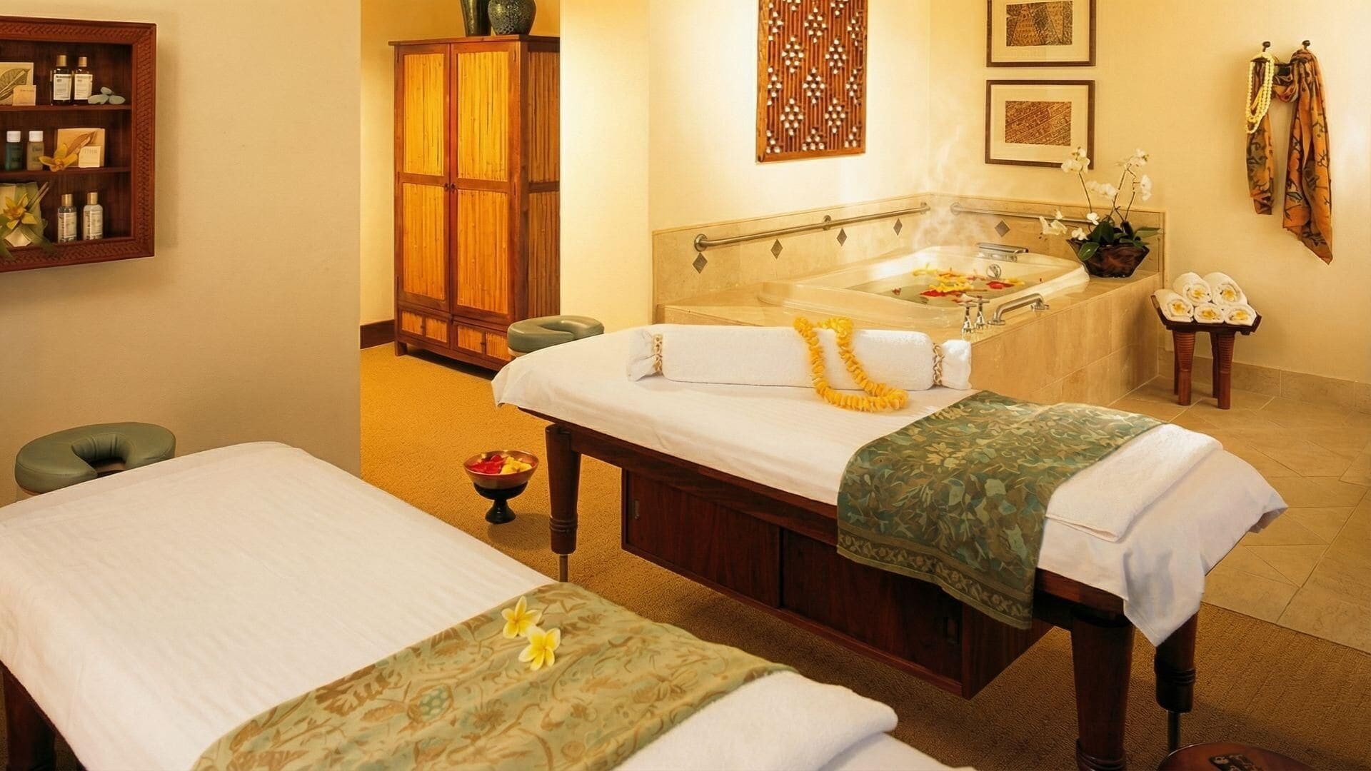 Een wellnessruimte met twee bedden, een massagetafel, een badkuip en een plank met toiletartikelen.