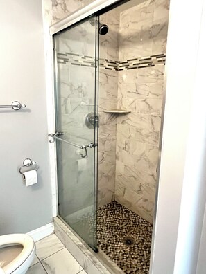 A glass-enclosed shower with a marble wall and a small shelf.