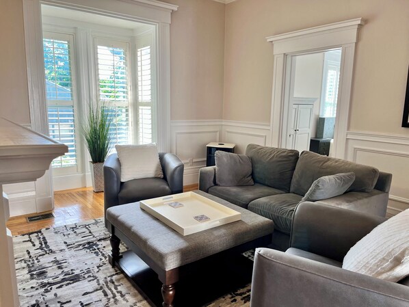 A living room with a grey sofa, a matching ottoman, a white coffee table, and a potted plant.